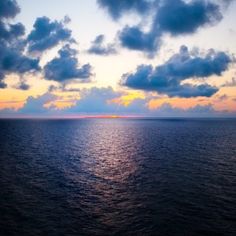 the sun is setting over the ocean with some clouds in the sky and blue water