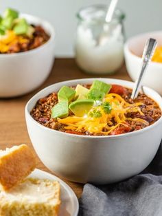 a bowl of chili with cheese and sour cream on the side next to two slices of bread