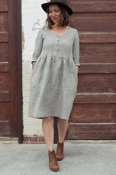 a woman standing in front of a brick wall wearing a hat and dress with buttons