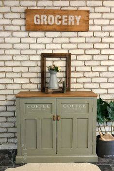 a green cabinet sitting in front of a brick wall next to a potted plant