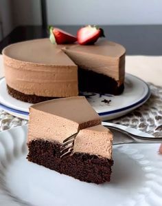 a piece of chocolate cake on a white plate with a fork and strawberry in the background