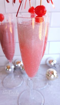 two glasses filled with pink liquid and topped with cherry garnish, sitting on a counter