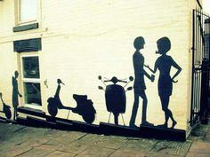 a mural on the side of a building depicting two people talking to each other and one person holding a scooter