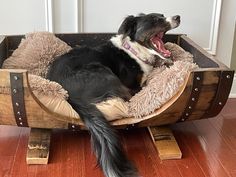 a black and white dog laying in a wooden bed on top of a hard wood floor