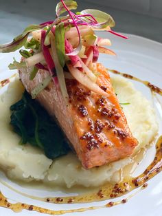 a white plate topped with salmon and mashed potatoes covered in sauce, garnished with radishes