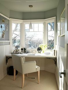 a white chair sitting in front of a window next to a desk with a computer on top of it