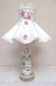 a white lamp with pink flowers on it and a small figurine next to it