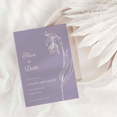 a purple and white wedding save the date card on a table with flowers in it