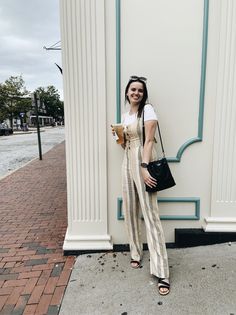 a woman standing next to a white building holding a black purse and smiling at the camera