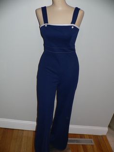 Great vintage 70's navy polyester knit jumpsuit. It is tight fitting and does have some stretch. The jumpsuit is accented with white across the top and stitches at the waist and blue buttons at the straps. The jumpsuit does up at the back with zipper and eyehook. The white jacket is accented with navy around the neckline and blues stitches. Ties at the front. No tags or labels. Measurements - shown on form unpinned with shoulders 14.5, bust 34, waist 23.5 and hips 34 Inches. Flat - bust 17 waist Navy Sleeveless Fitted Jumpsuits And Rompers, Fitted Retro Overalls, Fitted Overalls With Buttons For Workwear, Vintage Fitted Overalls For Workwear, Fitted Blue Jumpsuits And Rompers With Button Closure, Fitted Overalls With Button Closure, Fitted Overalls With Buttons, Vintage Fitted Blue Overalls, Vintage Blue Fitted Overalls