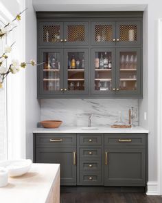 a kitchen with gray cabinets and marble counter tops, gold pulls on the doors, and wooden flooring