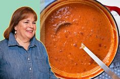 a woman standing in front of a large pot of chili sauce with a spoon sticking out of it