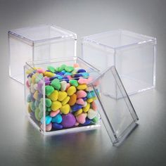 two clear boxes filled with colorful candies on top of a silver surface and one is empty