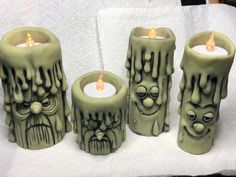 three green candles with faces on them sitting next to each other in front of a white towel