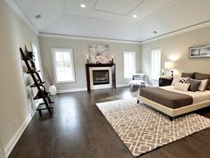 a large bedroom with hardwood floors and white walls, has a fireplace in the corner