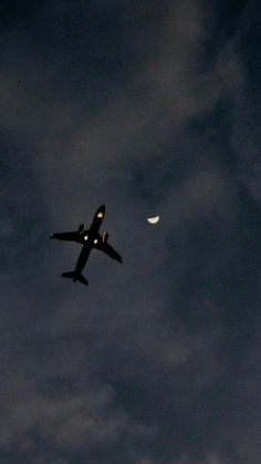 an airplane is flying in the sky at night with moon and clouds behind it on a cloudy day