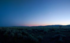 the sun is setting over an open field with mountains in the distance and blue sky