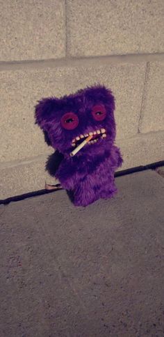 a purple stuffed animal sitting on the ground next to a brick wall with its mouth open