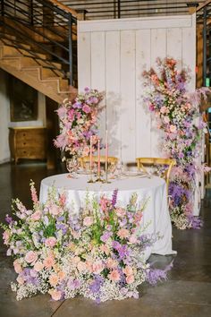 an arrangement of flowers and candles on a table in front of a wall with stairs