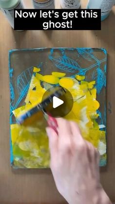 someone is painting yellow and blue leaves on a piece of paper with the words now let's get this ghost