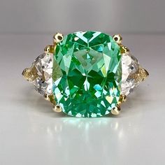 a green and white diamond ring with three diamonds on the side, set in yellow gold