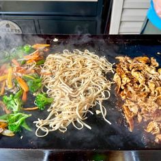 noodles, broccoli and carrots being cooked on a grill