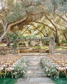 an outdoor ceremony set up with chairs and flowers on the aisle, surrounded by trees