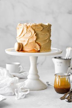 a cake sitting on top of a white cake plate next to cups and utensils