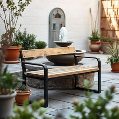 a wooden bench sitting on top of a patio next to potted plants and water fountain