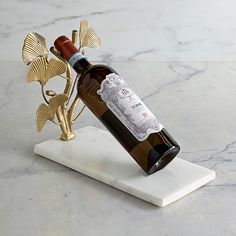 a bottle of wine sitting on top of a white marble table next to a gold flower