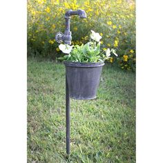 a metal bucket filled with flowers sitting on top of a grass covered field next to a faucet