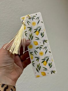 a hand holding a piece of paper with lemons on it and tassels