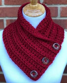 a red knitted cowl with two buttons on the front and bottom, sitting on a mannequin