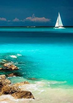 a sailboat in the ocean with rocks and water