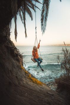 a woman swinging on a rope over the ocean