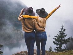 two women standing on top of a mountain with their arms in the air and looking out over a lake