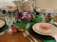 the table is set with plates, silverware and pink flowers on green placemats