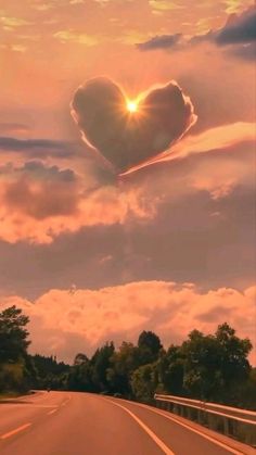 a heart shaped cloud in the sky above a road with trees and bushes on both sides