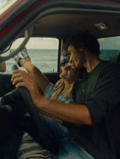 a man and woman sitting in the driver's seat of a car, looking at each other