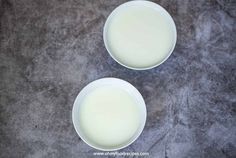 two white bowls filled with milk sitting on top of a gray countertop next to each other