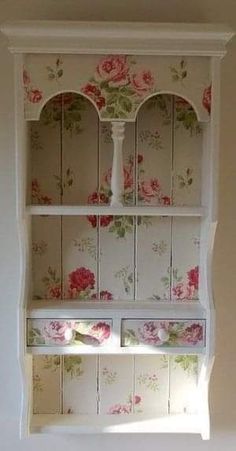 a white china cabinet with floral wallpaper and pink roses on the top, in a room