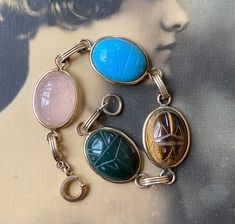 "This listing is for a vintage, stone scarab bracelet with a gold metal setting and gold filled clasp. Bracelet measures 7 3/8\" long.  Clasp is marked \"1/20 12K gold fill\". Stones are a nice large size and measure approx. 20mm x 15mm. Clasp is in good working condition. All the scarabs are some type are stones; bloodstone, tigereye, pink quartz and pretty blue chalcedony.  No obvious chips or cracks in the stones. Thanks." Antique Oval Gemstone Bracelets, Vintage Agate Bracelet, Antique Gold Cabochon Bracelets, Vintage Yellow Gold Cabochon Bracelets, Gold-tone Metal Bracelet With Toggle Clasp, Scarab Bracelet Vintage, Scarab Bracelet, Handmade Vintage Agate Beads, Gems, And Cabochons, Clasp Bracelet