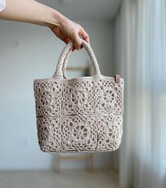 a hand holding a crocheted bag in front of a window