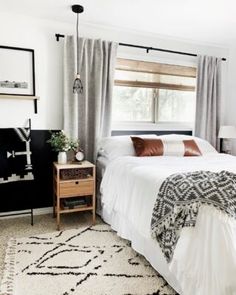 a bedroom with a white bed, black and white rugs, gray drapes, brown pillows