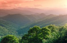 the mountains are covered in lush green trees and grass as the sun sets over them