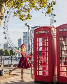 a woman in a red dress is walking past two red telephone booths and a ferris wheel