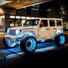 a white jeep parked in front of a building at night with blue lights on it's tires