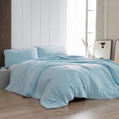 a bed with blue sheets and pillows in a white room next to a wooden floor