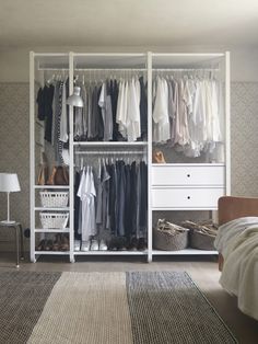 a white closet with clothes and baskets on the bottom shelf, next to a bed