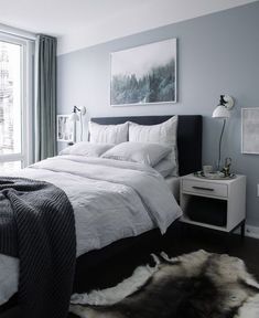 a bed with white sheets and pillows in a bedroom next to a window, rugs and pictures on the wall